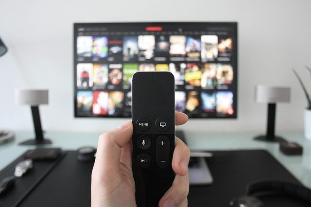 A person holding a remote control in front of a television.